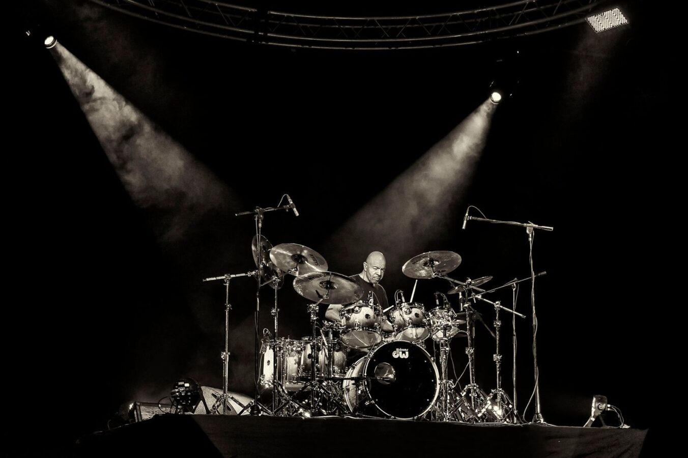 Baterista tocando bajo dos focos de luz en un escenario oscuro