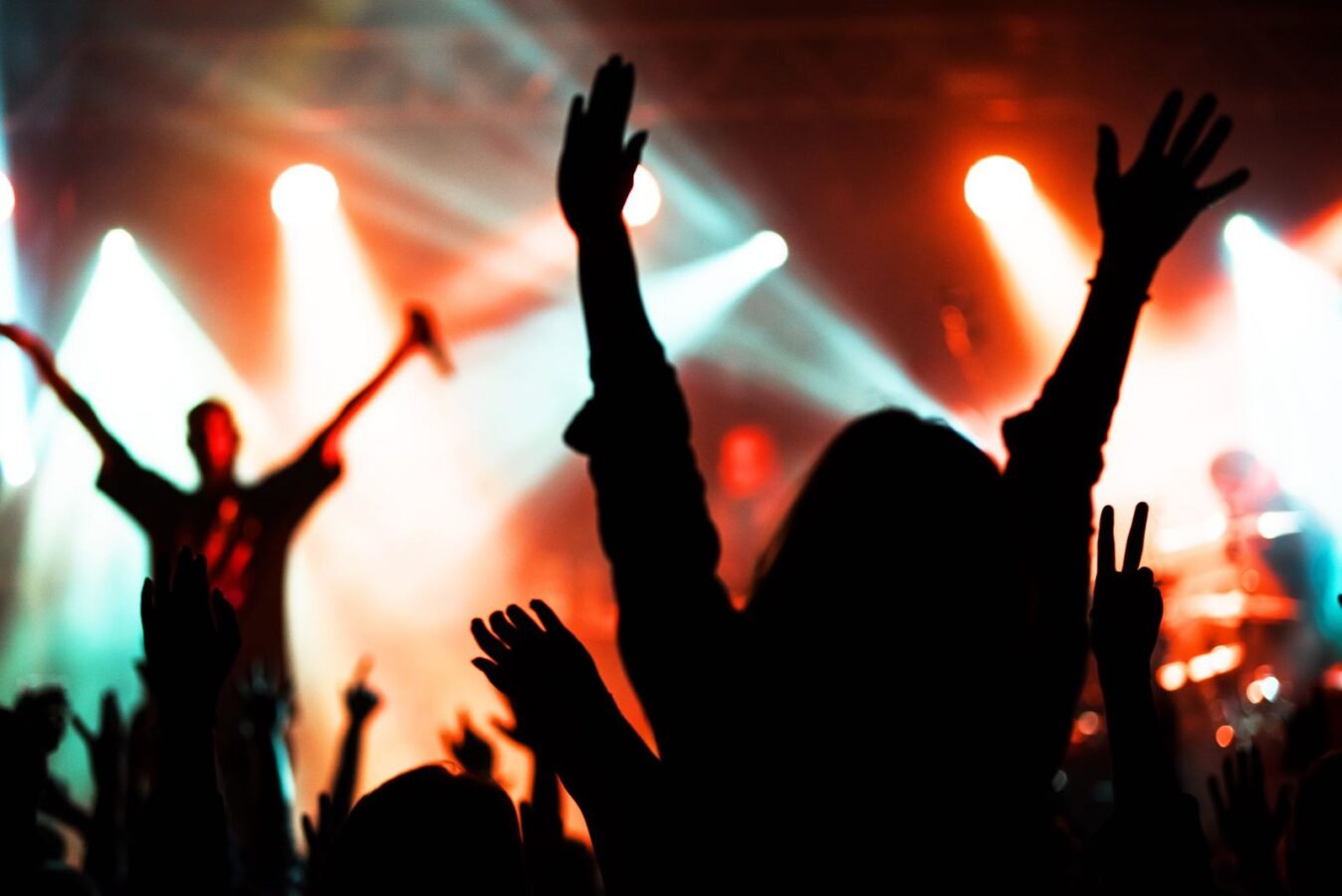 Público com os braços para cima diante de um palco com luzes coloridas