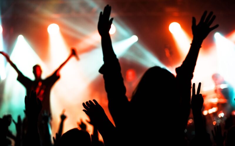 Público com os braços para cima diante de um palco com luzes coloridas