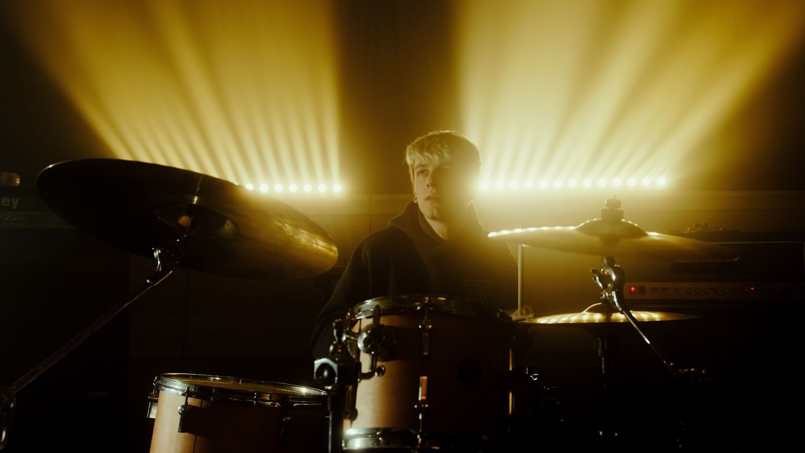 Drummer behind his kit with beams of yellow light in the background