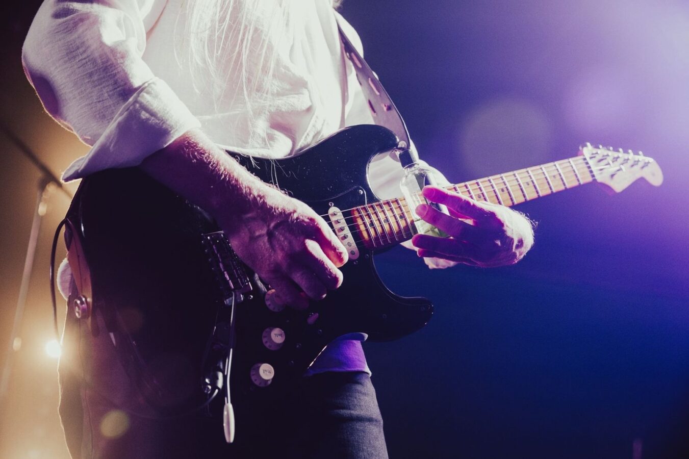 Guitarrista tocando guitarra elétrica em um palco com luzes roxas