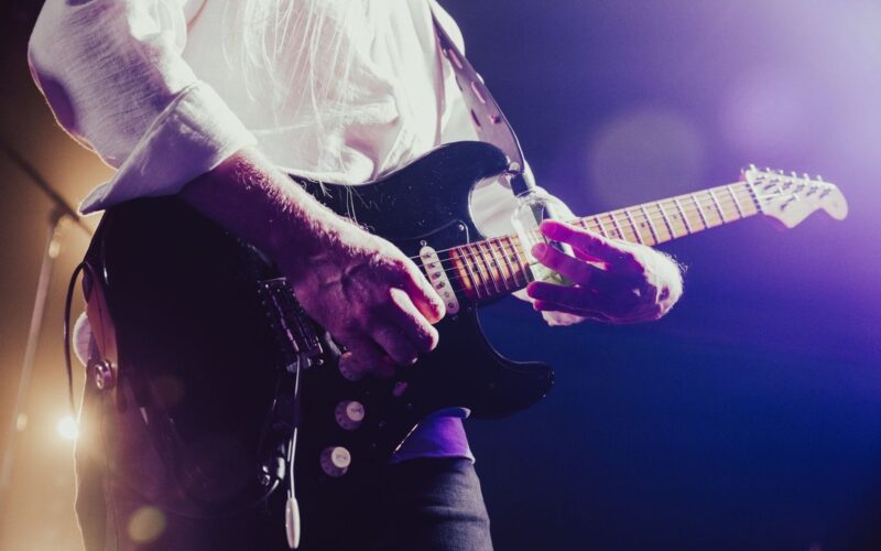 Guitarist playing an electric guitar on a stage with purple lights